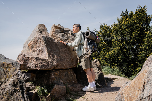 Young short haired female hiker with backpack and travel equipment looking  away while standing Stock Photo by LightFieldStudios