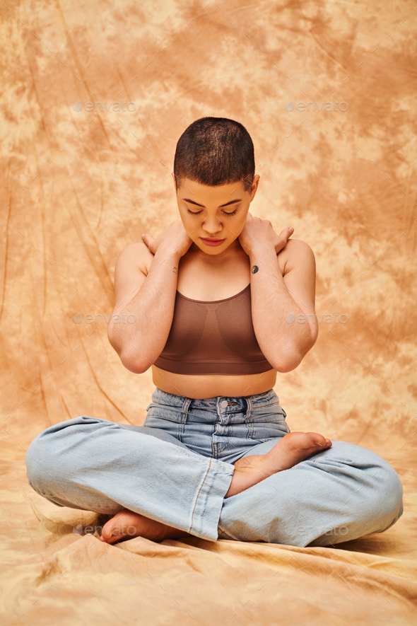 body confidence, relaxation, curvy young and tattooed woman in jeans and crop top sitting