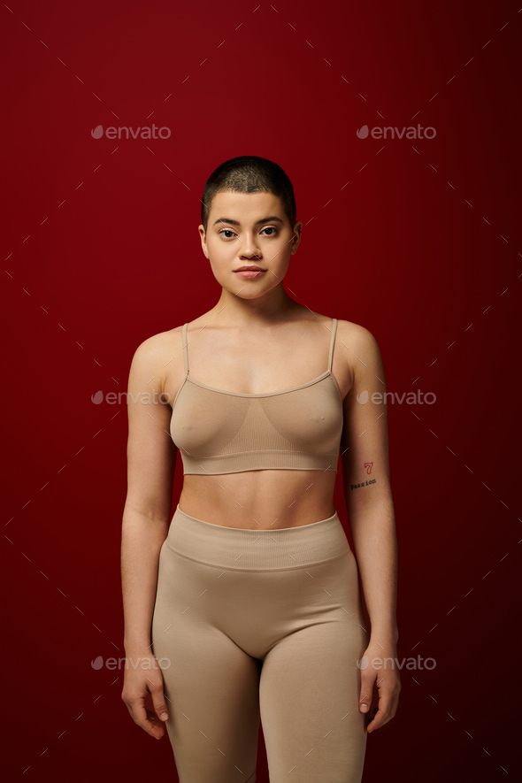 body diversity, young tattooed woman in beige underwear posing on red  background, body positivity, Stock Photo by LightFieldStudios