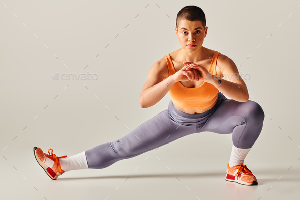 self-esteem, body positivity, flexible and short haired woman stretching legs on grey background,