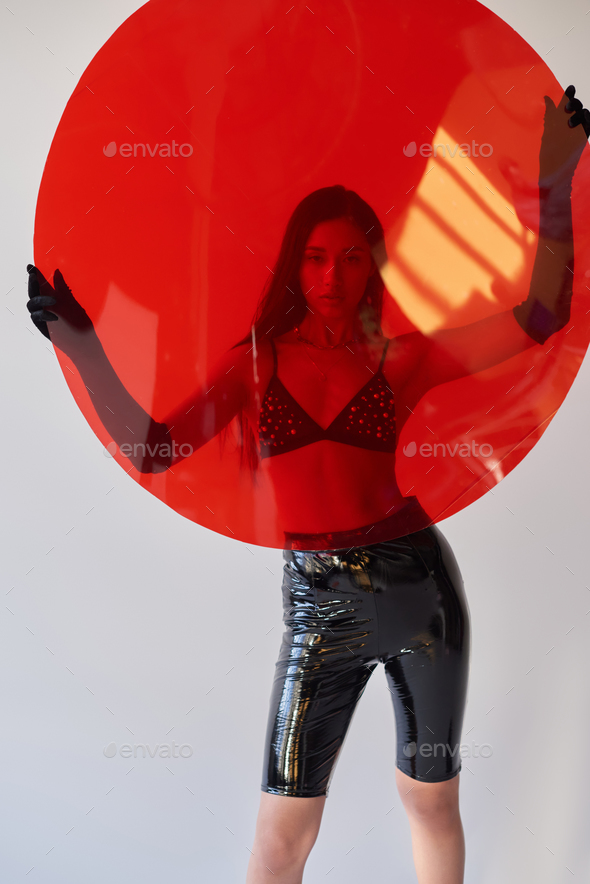 beauty and fashion, latex style, young asian woman in bra and gloves  holding red round shaped glass Stock Photo by LightFieldStudios
