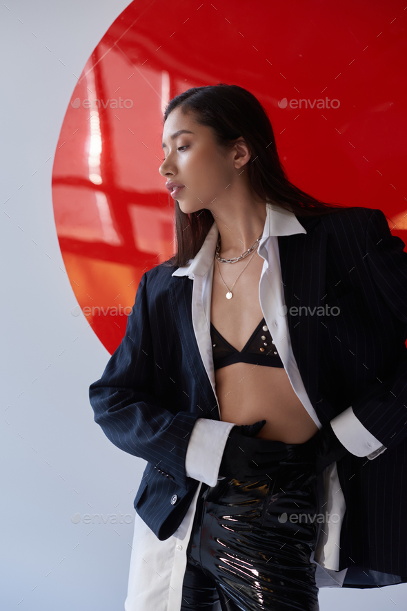edgy fashion, young asian woman in bra, white shirt and blazer posing in  latex pants and black Stock Photo by LightFieldStudios