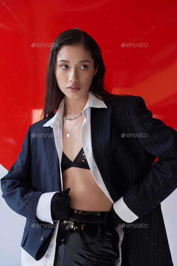 modern fashion, young asian woman in bra, white shirt and blazer posing in  gloves near red round Stock Photo by LightFieldStudios