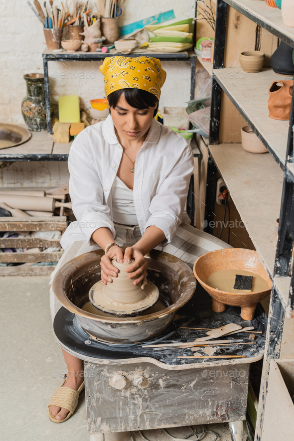 Young asian female artisan in headscarf in workwear molding clay on pottery  wheel near bowl Stock Photo by LightFieldStudios