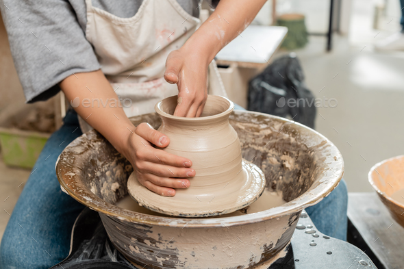 Cropped view of young female potter in apron molding clay vase and working  with spinning pottery Stock Photo by LightFieldStudios