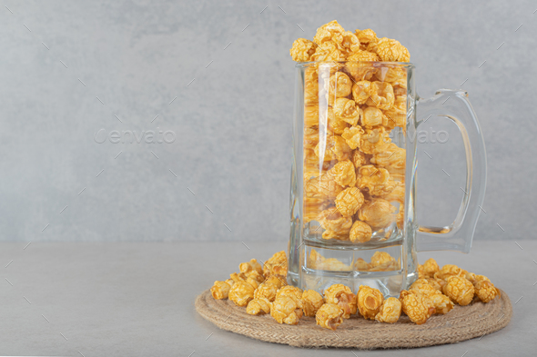 Full glass mug on a trivet ringed with caramel flavored popcorn on marble background
