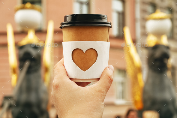 cup of natural coffee with carved white heart in woman\'s palm on bridge in St. Petersburg