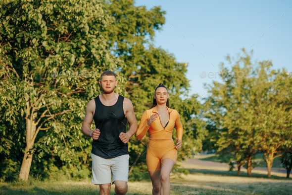 Running in Sync Male Personal Trainer Motivates Female Athlete Outdoors