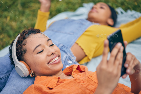 Music, phone and lesbian couple relax at picnic on grass, technology and streaming service app in n