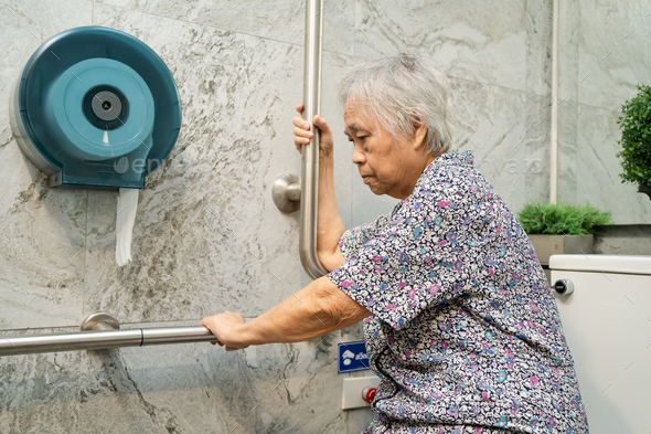 Asian senior woman patient use toilet bathroom handle security in nursing hospital.