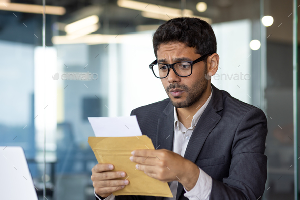 Upset and disappointed businessman at workplace received mail message envelope letter with bad news