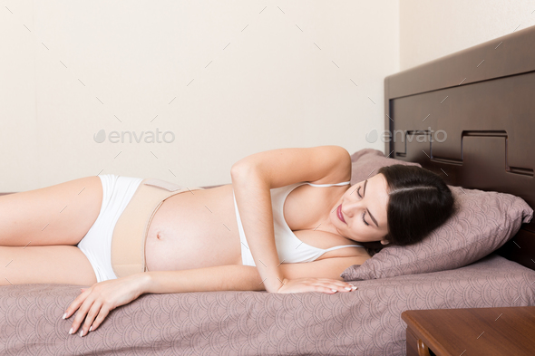 closeup pregnant woman dresses bandage on belly at home on bed. Orthopedic abdominal support belt