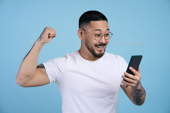asian man holding mobile phone sports betting, win money isolated on blue background