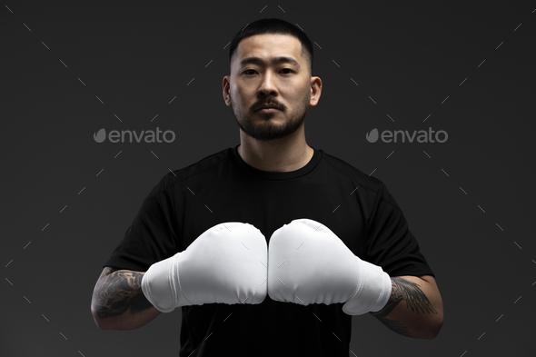 Asian man, boxer wearing white boxing gloves, looking at camera isolated on black background