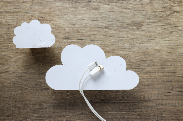 White, paper clouds with a white USB cable on a wooden background