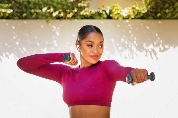 Athletic african american sportswoman exercising with dumbbells outdoor
