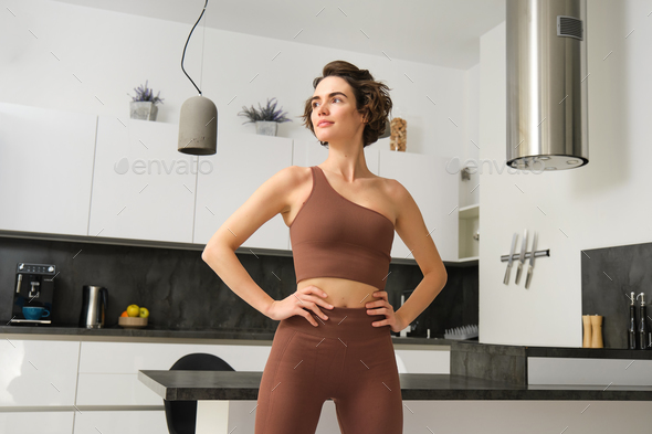 Image of young fit woman, fitness girl in sportswear, standing in power pose, workout at home