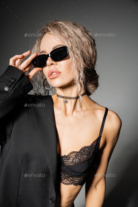 portrait of stunning and sexy woman in lace bra, trendy necklace and blazer  adjusting dark Stock Photo by LightFieldStudios