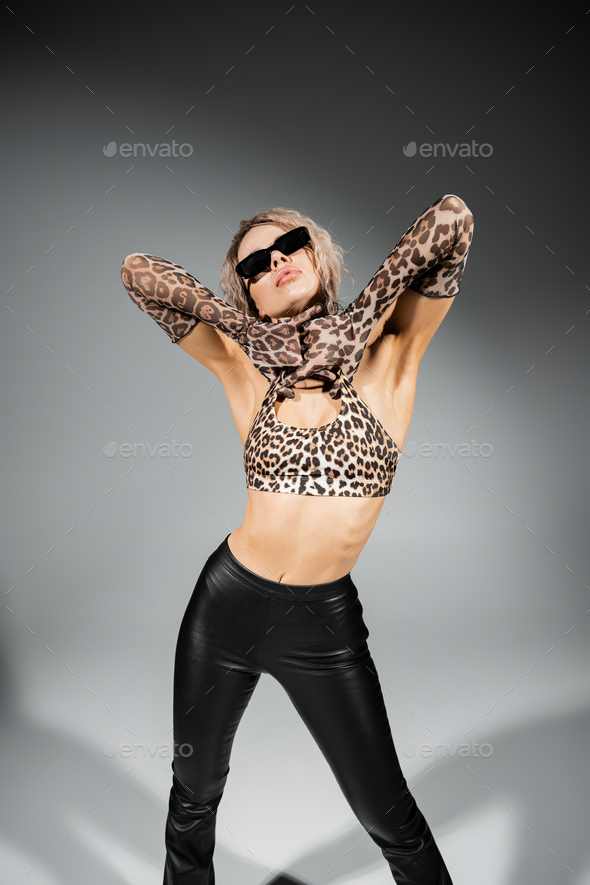 appealing woman in dark sunglasses, animal print crop top, long gloves and black latex pants