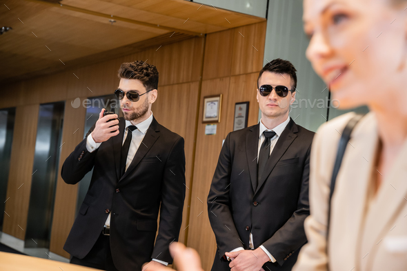handsome bodyguards protecting beautiful and successful client in hotel, blonde woman on blurred