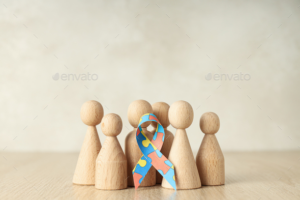 Ribbon with colorful puzzle pieces and wooden figures on light background. World autism day concept
