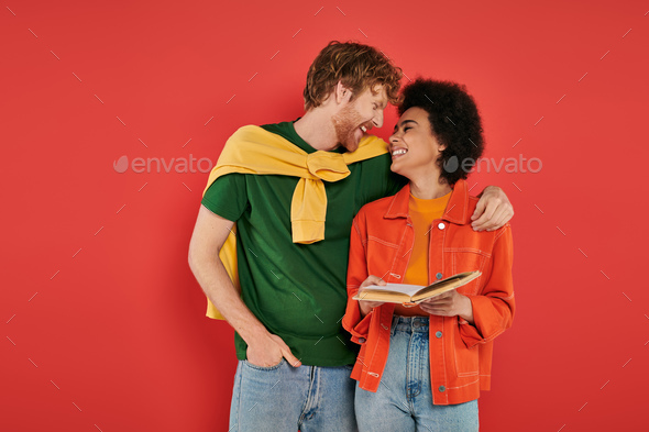 interracial couple hugging and reading book on coral background, cultural diversity, vibrant