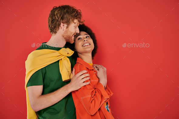 interracial couple hugging and smiling on coral background, cultural diversity, vibrant colors,