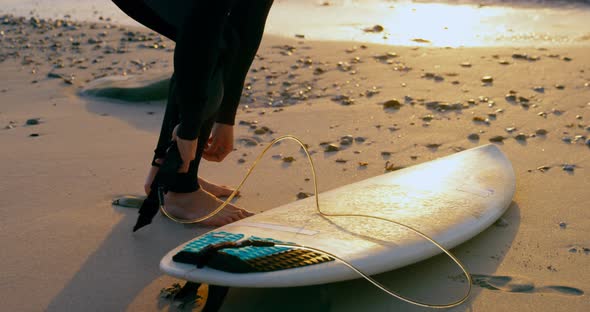 Side view of mid-adult caucasian male surfer tying surfboard leash at the beach 4k alt