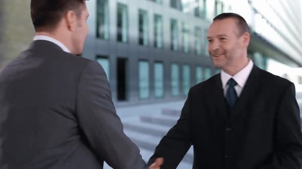 Businessmen shaking hands as they walk past each other alt
