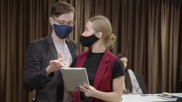 Young Man and Woman in Coronavirus Face Masks Talking Discussing Business Idea and Looking at Camera alt