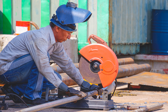 Asian welder using fiber cutting machine to cut galvanized steel pipes in outdoor workshop area