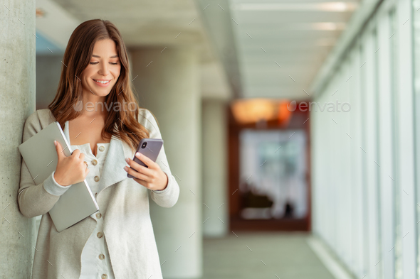 Smiling woman, worker holding mobile phone, laptop working online, check email in modern office