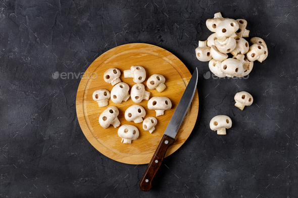 Cutting board with fresh wild mushrooms in the form of skulls and knife on white table.