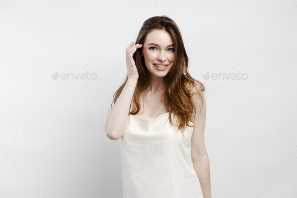 Smiling sexy woman in nightgown fixing hair, looking at camera