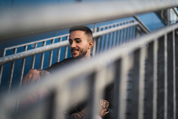 Smiling young hot man sitting on a staircase - a view through handrails ...