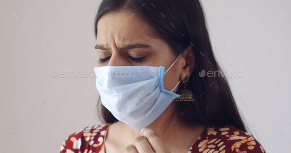 Young Indian female wearing a face mask, coughing and feeling bad