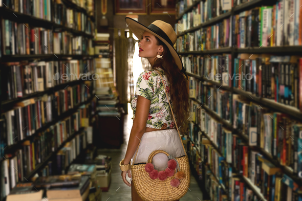 Beautiful girl wearing stylish outfit looking for interesting book in the vintage bookstore