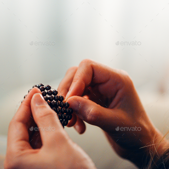 Closeup of hands of a bead master making jewelry from black round beads