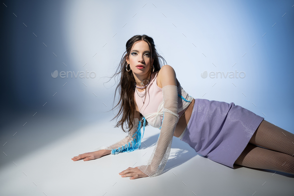 Trendy young asian woman in mesh top and skirt looking at camera while posing on blue background