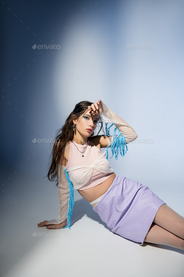 Fashionable young asian woman in mesh top and skirt looking at camera on blue background