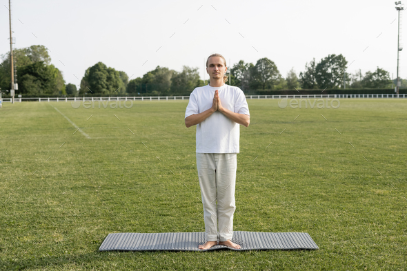 full length of barefoot man in linen pants meditating in mountain pose with praying hands on yoga