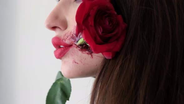 Beautiful Brunette with Stylish Makeup with Blood and Rose in Her Mouth alt