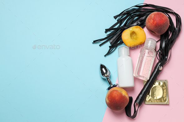 Lubricant with a whip, a peach and a condom on a blue-pink background, place for text