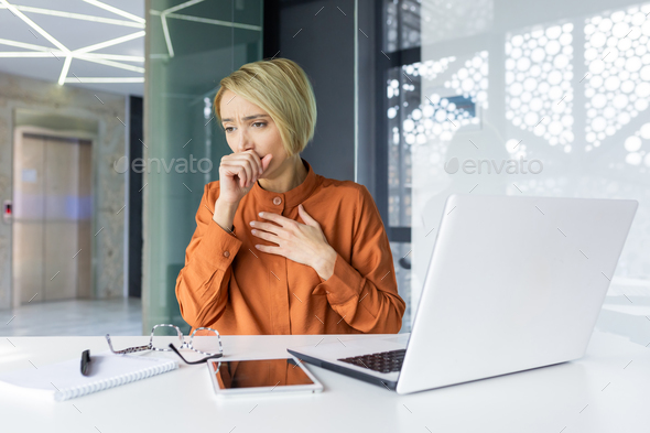 Sick cold woman at workplace, coughing, businesswoman sitting at desk with laptop inside office