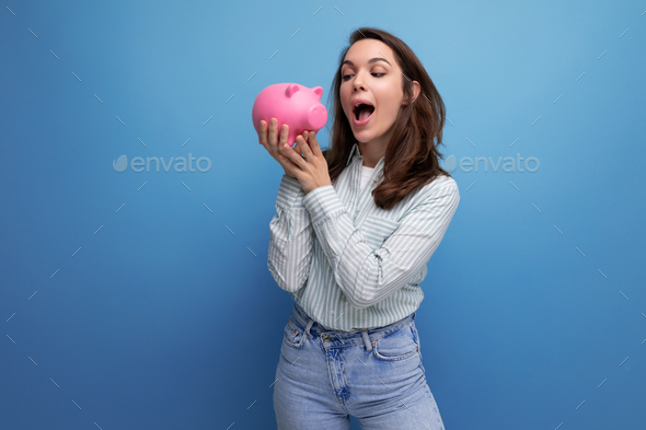smiling attractive european brunette young lady keeps money in a pink piggy bank
