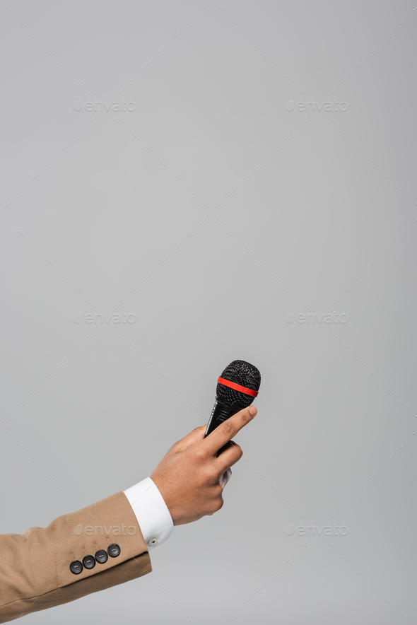 Cropped view of hand of event host in brown jacket holding wireless microphone during performance