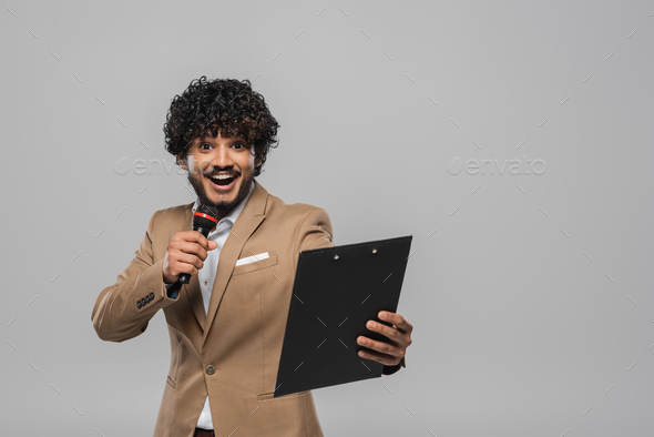 Cheerful and young indian host of event with curly hair standing in formal wear talking