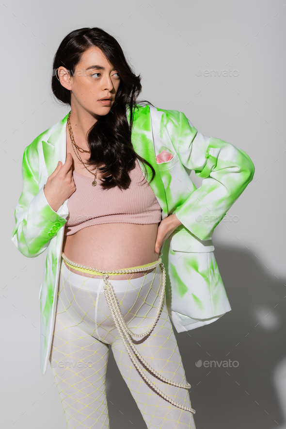brunette pregnant woman in green and white blazer, crop top, beads belt and leggings holding hand