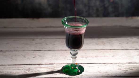 Seamless, looping clip of red wine pouring into a rustic glass with blue background. alt