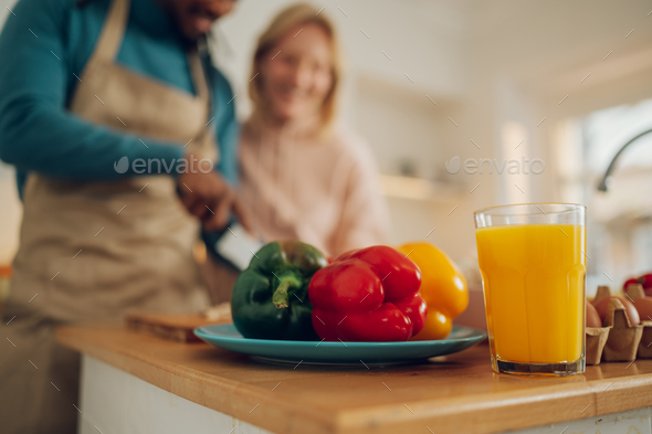 Close up of vegetables and juice on the kitchen counter at home with an interracial couple cooking.